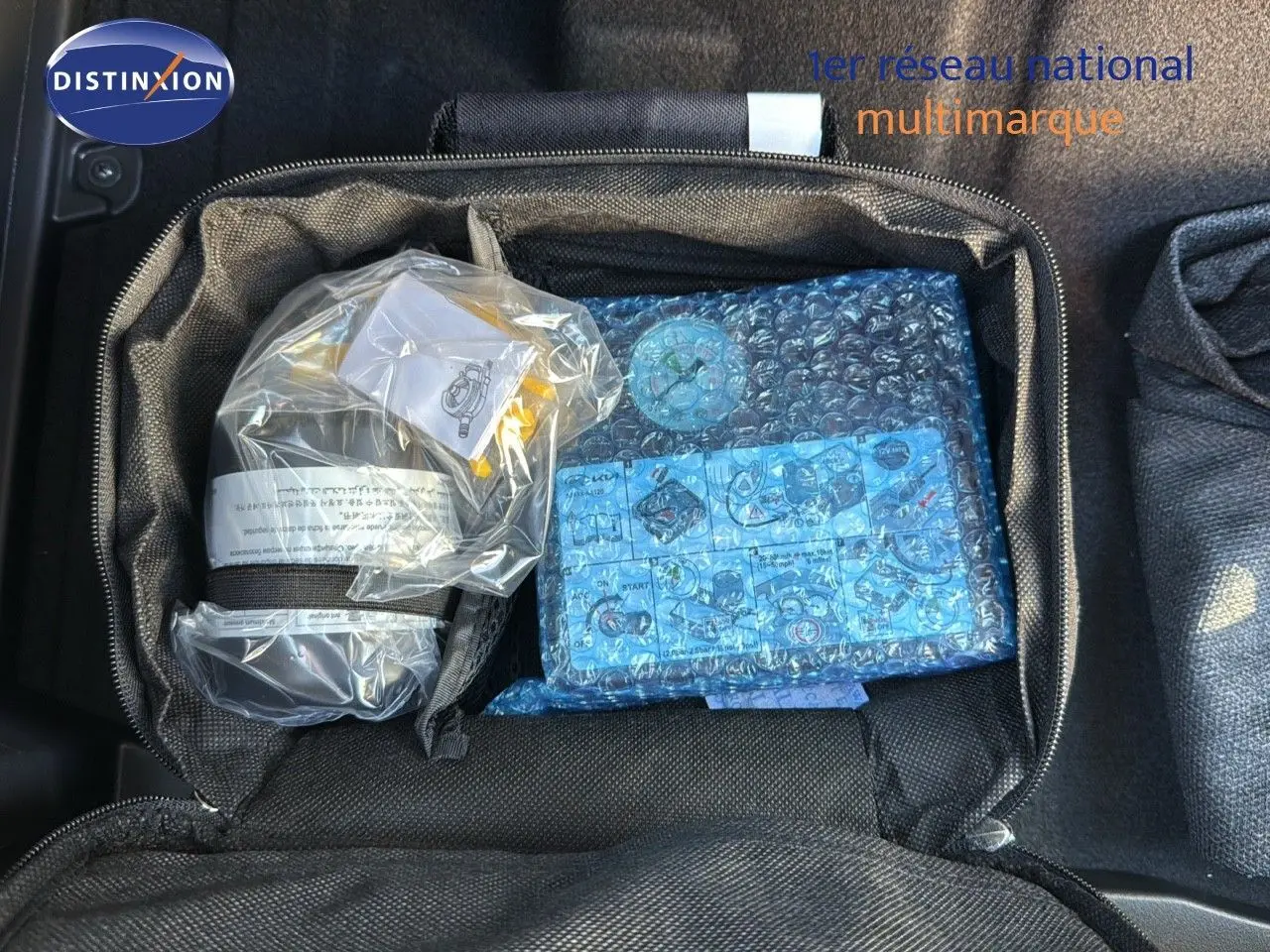 Sac de rangement noir ouvert dans le coffre d'une Kia Niro bleu minéral, contenant des accessoires emballés.