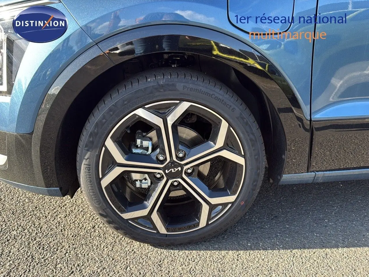 Gros plan sur la roue avant gauche d'un Kia Niro bleu minéral métal 2025 avec jante alliage bicolore.