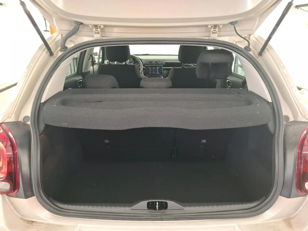 Coffre ouvert d'une Citroën C3 beige clair vue arrière, montrant l'intérieur noir et tablette cache-bagages.