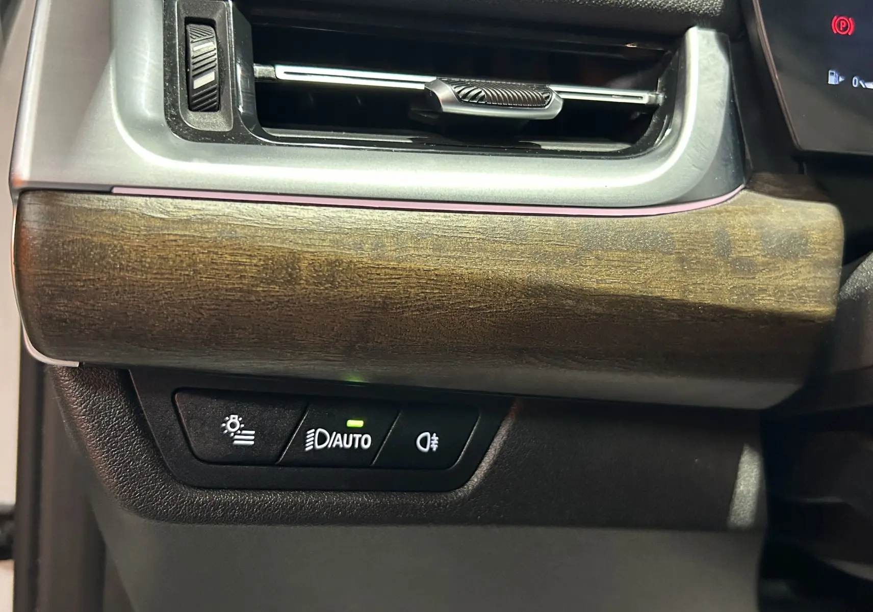Détail du tableau de bord avec insert en bois et commandes d'éclairage sur une BMW Série 2 Active Tourer 218i blanche.