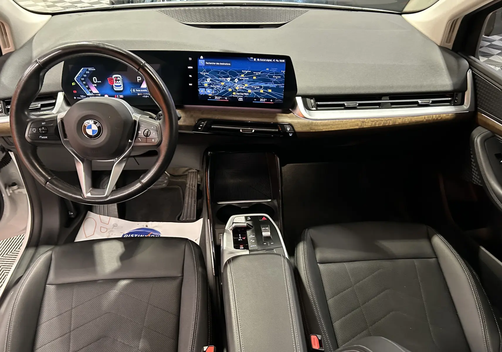 Vue intérieure avant de la BMW Série 2 Active Tourer 218i 2022, sièges cuir noirs et écran GPS central lumineux.