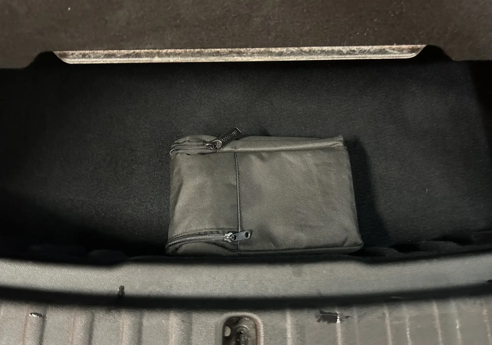 Vue plongeante sur le coffre ouvert d'une BMW Série 2 Active Tourer blanc, avec une trousse noire zippée à l'intérieur.
