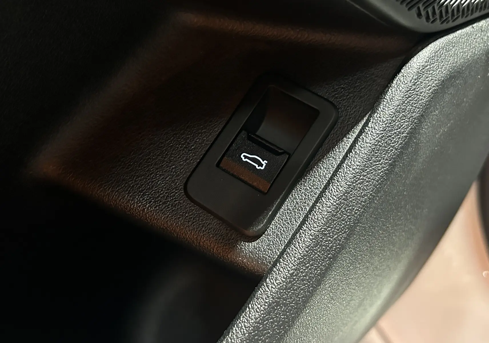 Gros plan sur le bouton d'ouverture électrique du hayon dans l'habitacle d'une BMW Série 2 Active Tourer blanche.