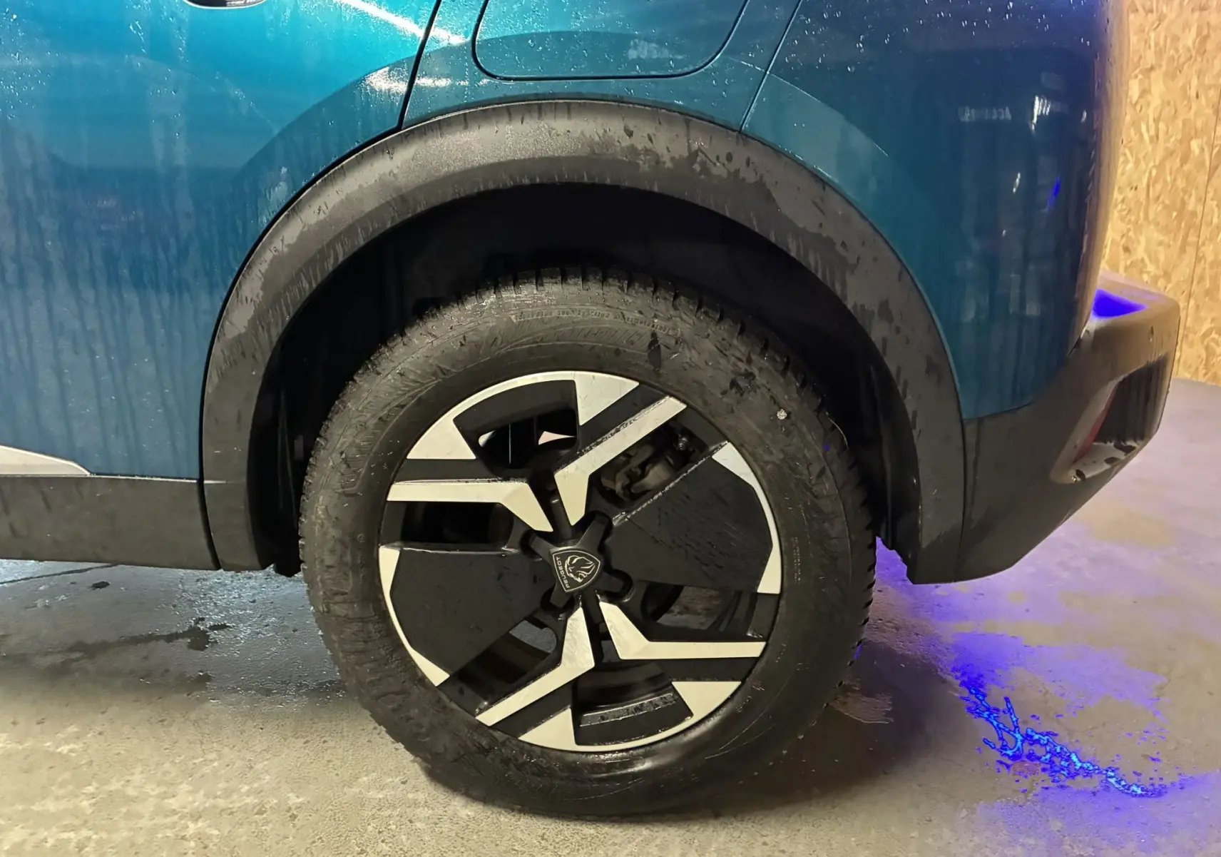 Gros plan sur la roue arrière droite d’un Peugeot 2008 bleu 2025, avec jante noire et argent au design moderne.