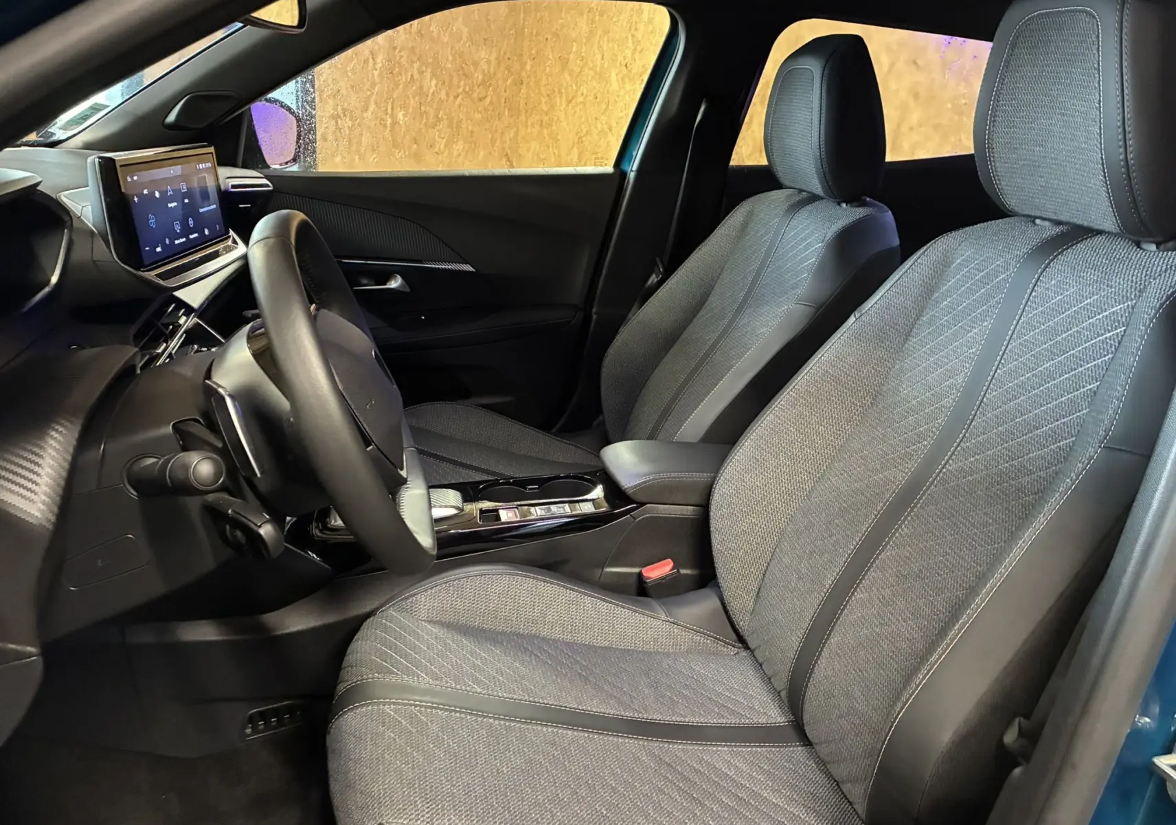 Vue intérieure côté conducteur du Peugeot 2008 bleu 2025, mettant en valeur les sièges tissu gris et le tableau de bord moderne.
