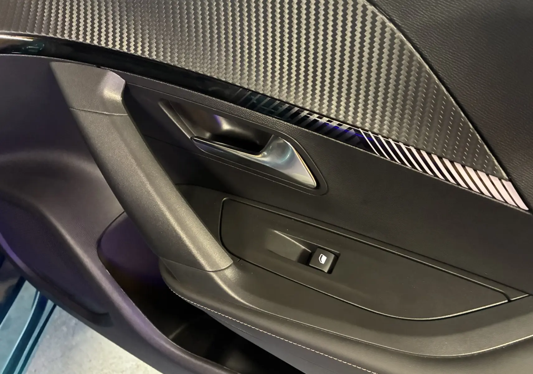 Détail de la porte intérieure côté gauche de la Peugeot 2008 1.2 Hybrid 136 Allure avec insert décoratif noir à effet carbone.