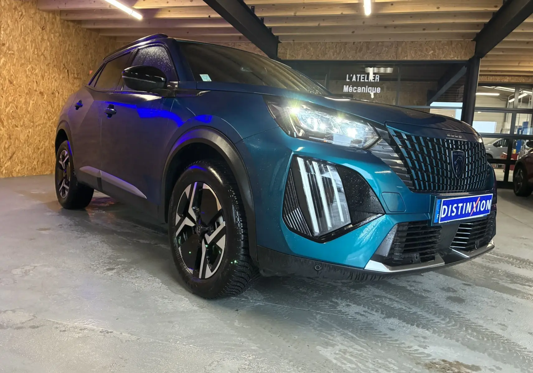 Vue 3/4 avant droit d'un Peugeot 2008 bleu hybride 2025 avec phares LED et calandre distinctive, stationné en intérieur.