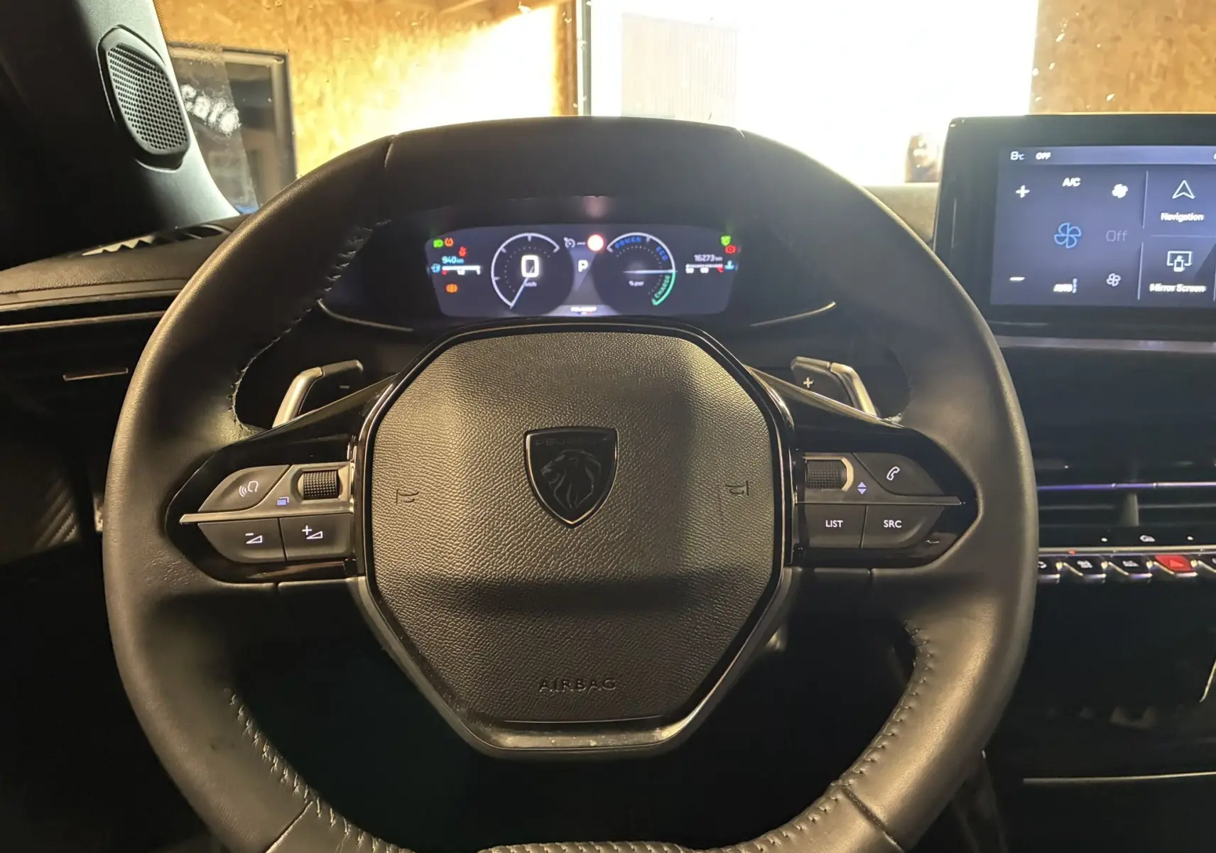 Vue rapprochée du volant cuir noir de la Peugeot 2008 1.2 Hybrid 136, avec tableau de bord numérique et écran tactile.