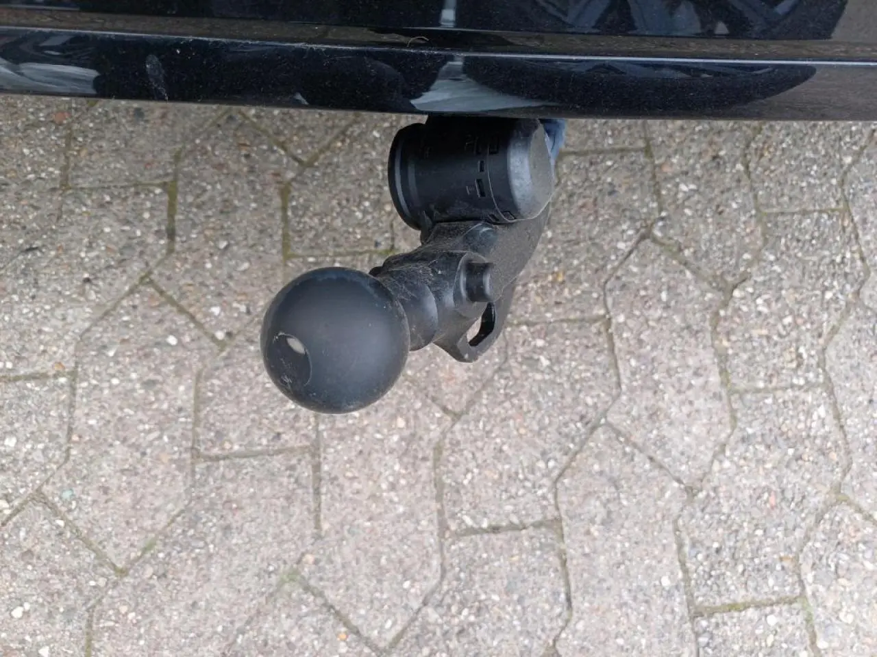 Gros plan sur l'attelage escamotable noir sous le pare-chocs arrière de la Volkswagen Golf 1.5 eTSI noire.