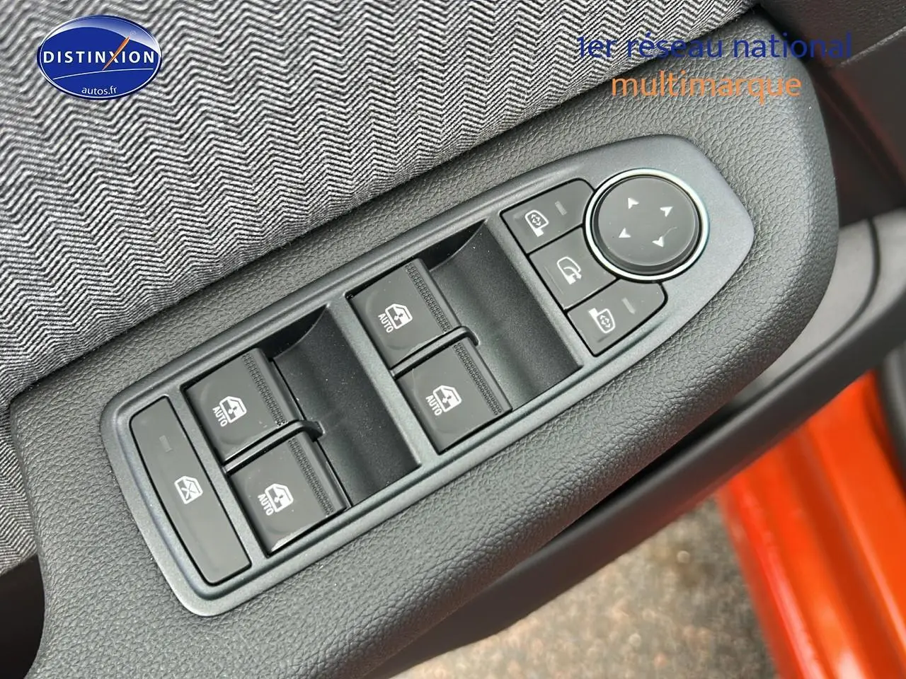 Gros plan sur les commandes des vitres et rétroviseurs côté conducteur d'une Renault Clio V orange Valencia.