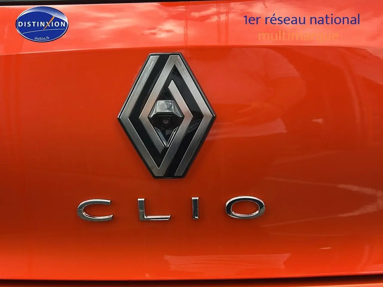 Gros plan sur le logo Renault et le badge Clio sur la malle arrière orange Valencia d'une Clio V hybride.