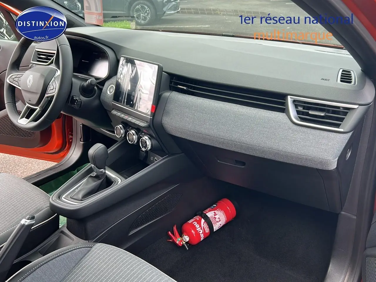 Intérieur avant droit de la Renault Clio V orange Valencia, tableau de bord moderne avec écran tactile et extincteur au sol.