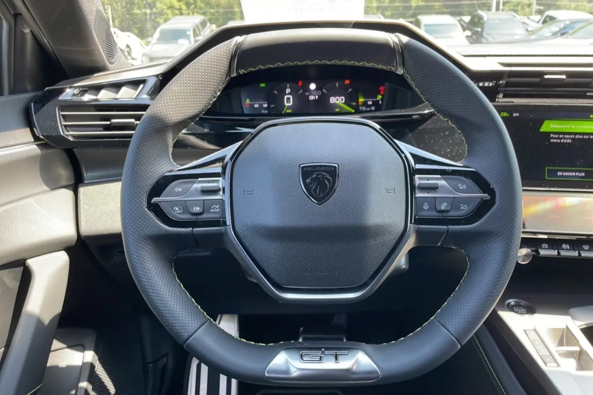Vue rapprochée du volant cuir perforé de la Peugeot 308 GT 2025 avec logo lion et badge GT visible.