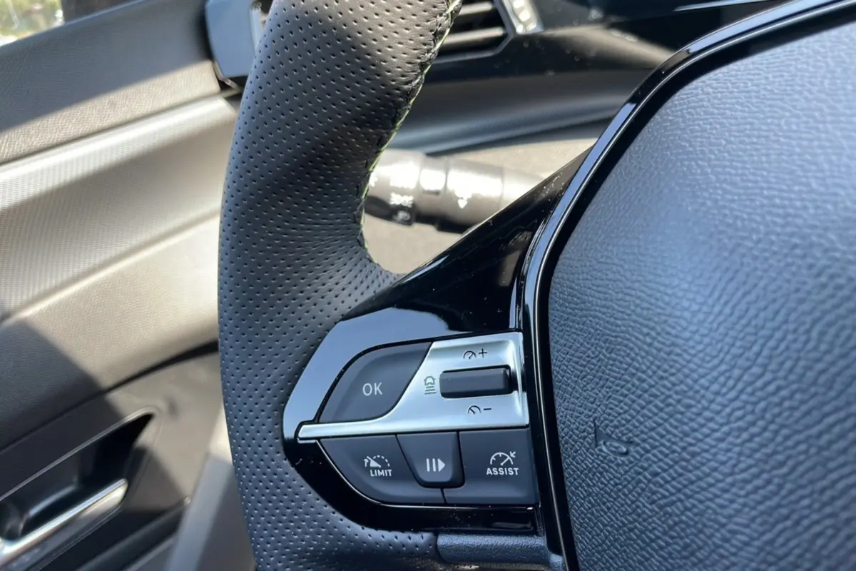 Gros plan sur le volant perforé noir de la Peugeot 308 1.5 HDI 130 EAT8 GT 2025, avec commandes intégrées et finition brillante.