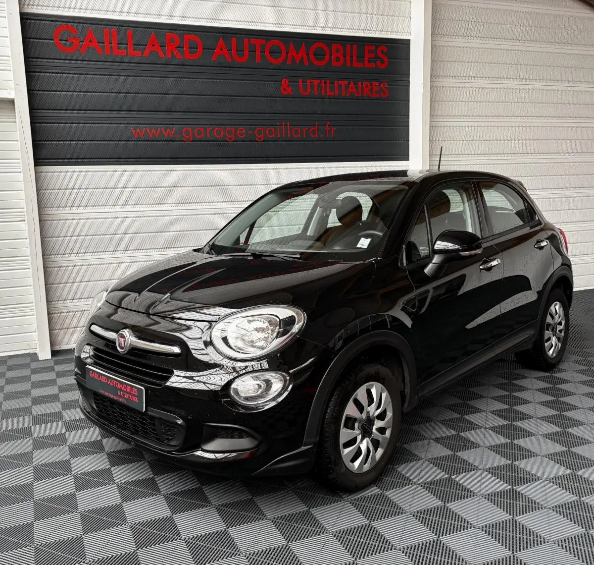 Vue 3/4 avant droit d'une Fiat 500X noire 2018 dans un garage avec sol carrelé gris et blanc.