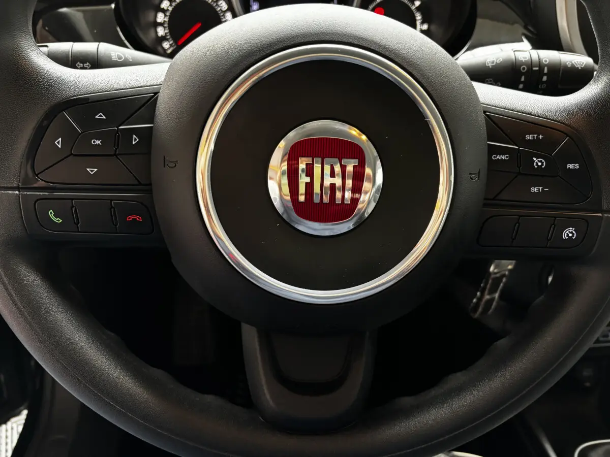 Gros plan sur le volant noir multifonctions avec logo FIAT rouge au centre du Fiat 500X 2018.