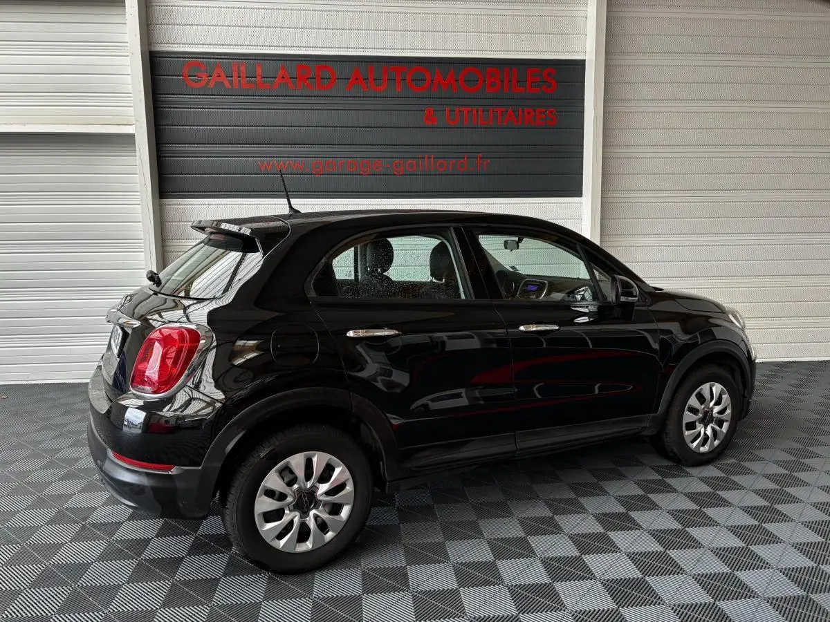 Vue de profil côté gauche d'une FIAT 500X noire 2018 garée en intérieur avec jantes argentées et feux arrière rouges.