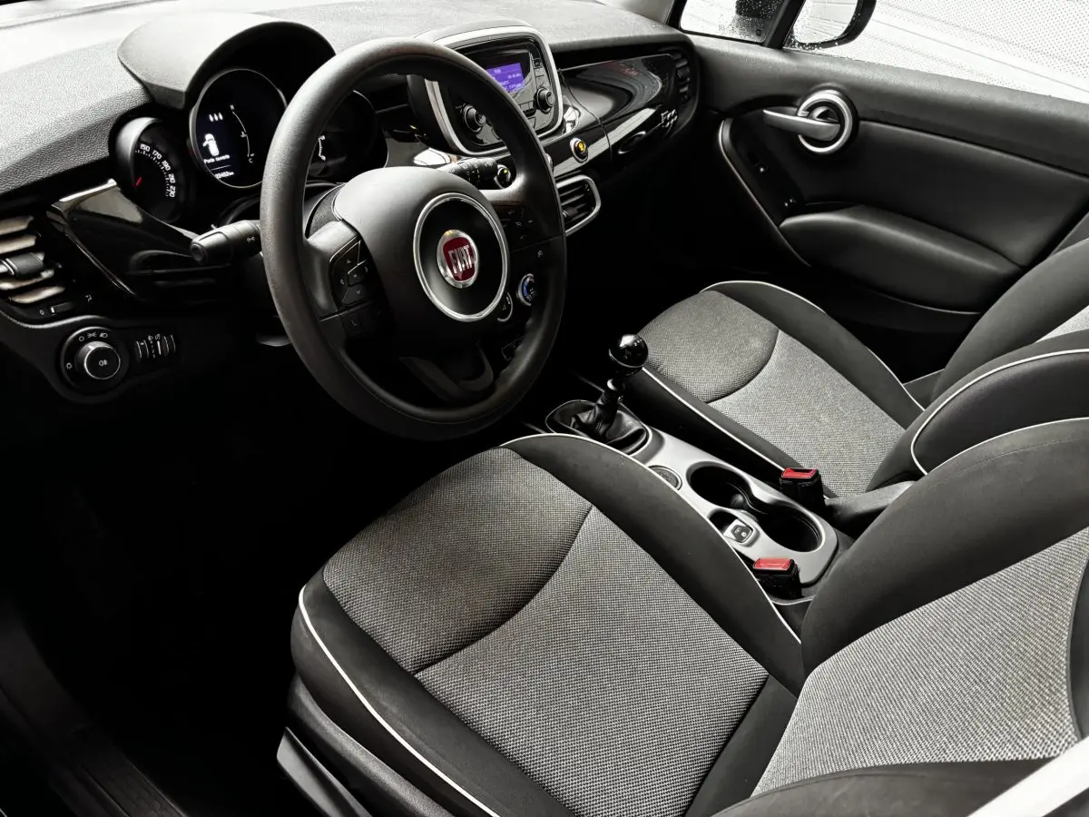 Vue intérieure côté conducteur de la Fiat 500X noire, montrant le volant multifonctions et la console centrale avec boîte manuelle.