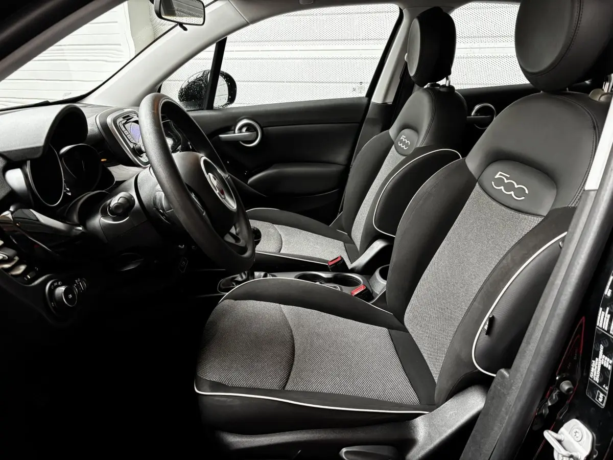 Vue intérieure côté conducteur de la Fiat 500X noire, sièges bi-matière avec logo 500 brodé sur appuie-têtes.