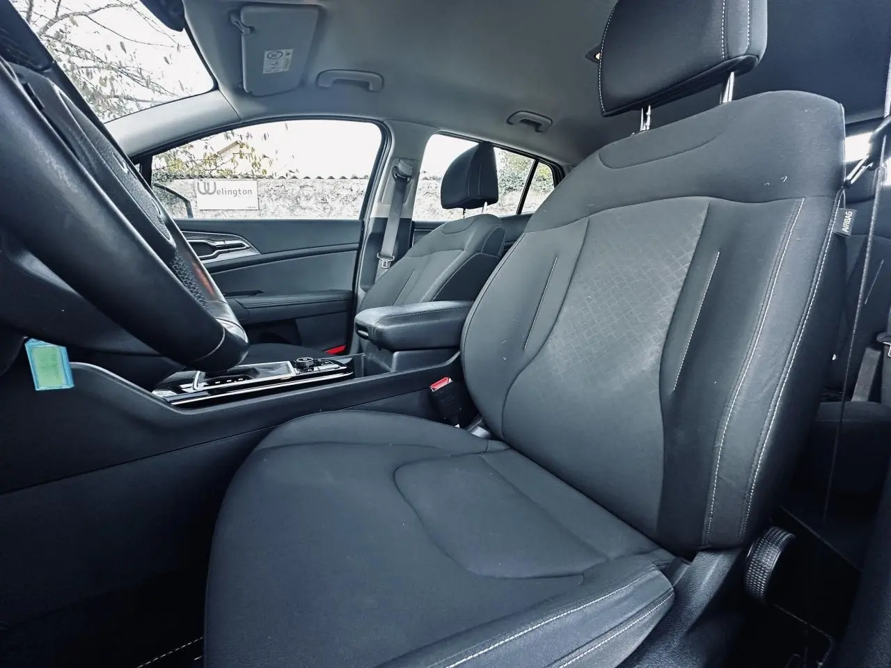 Vue intérieure côté conducteur du Kia Sportage 2023 noir, siège tissu avec accoudoir central et volant partiel visible.