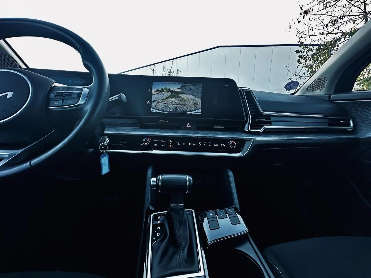 Vue intérieure du tableau de bord noir du Kia Sportage 2023 avec écran tactile affichant la caméra de recul et levier de boîte automatique.