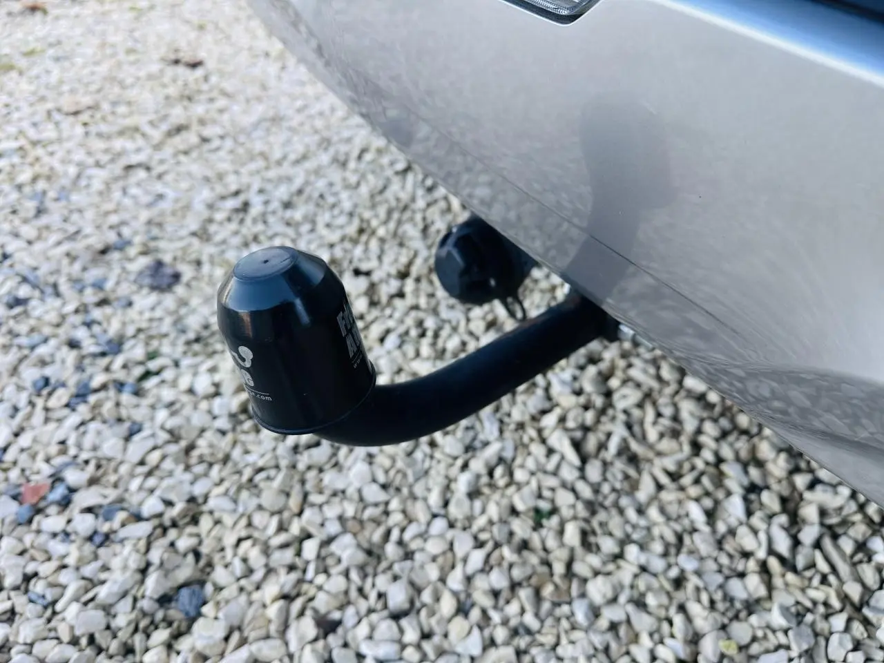 Gros plan sur l'attelage noir fixé à l'arrière d'un Kia Sportage noir, avec fond de gravier clair.