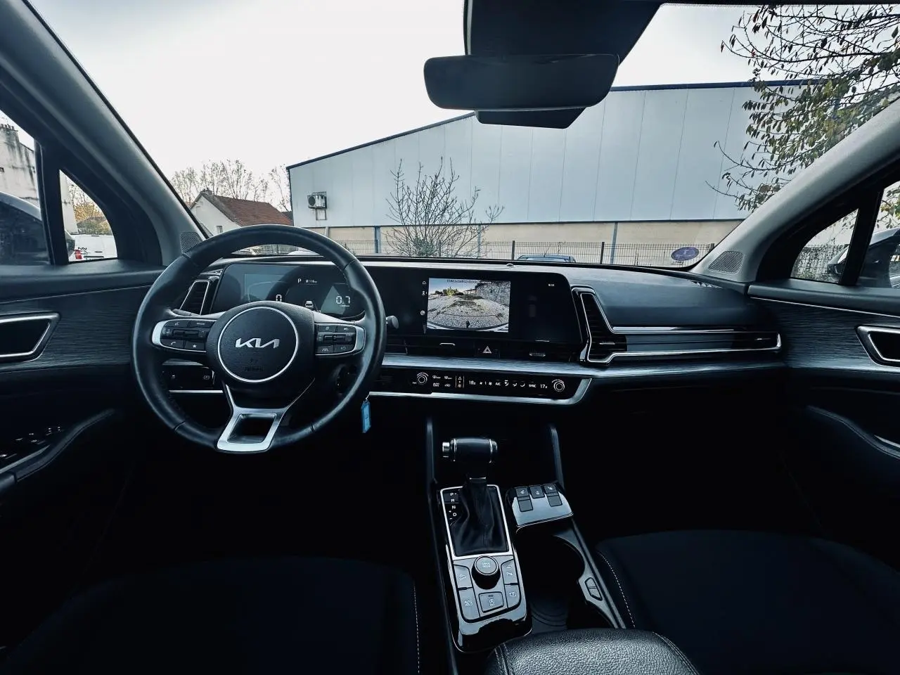 Intérieur noir du Kia Sportage 2023 vu de face, avec tableau de bord moderne et écran tactile affichant la caméra de recul.