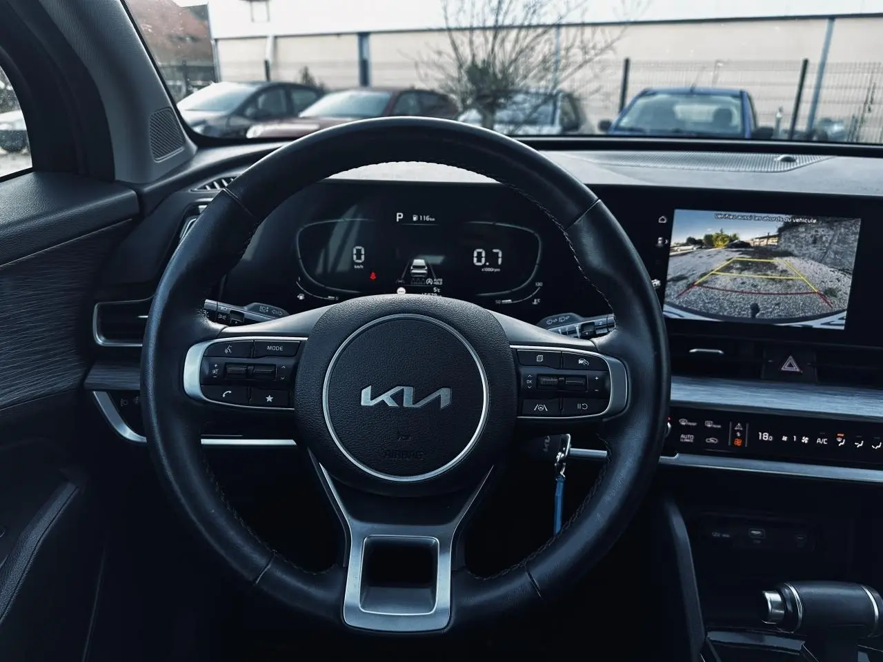 Vue intérieure centrée sur le volant KIA et l'écran tactile affichant la caméra de recul du Kia Sportage noir 2023.