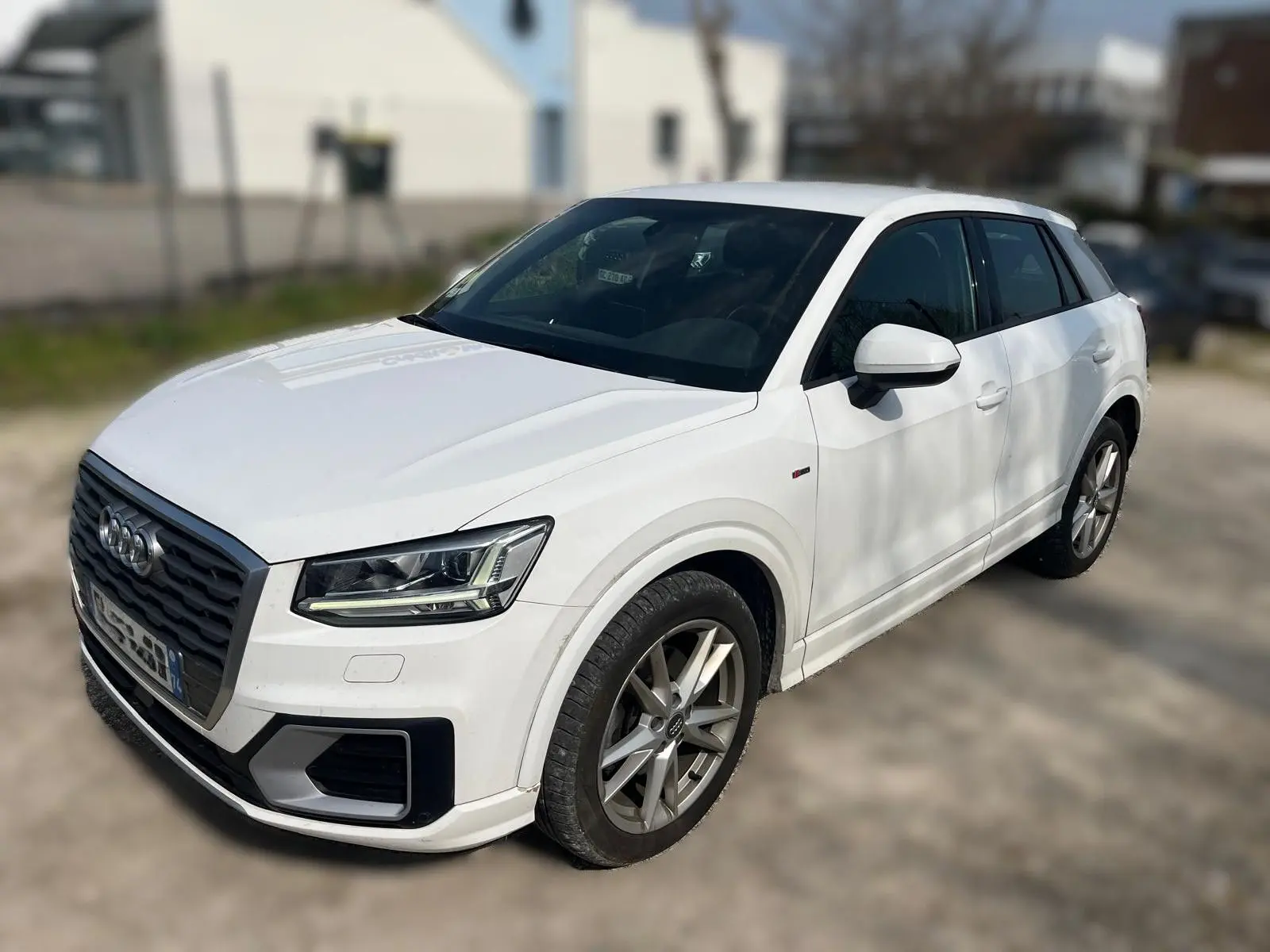 Audi Q2 blanc vue 3/4 avant droit, avec jantes alliage et calandre noire distinctive S-Line.