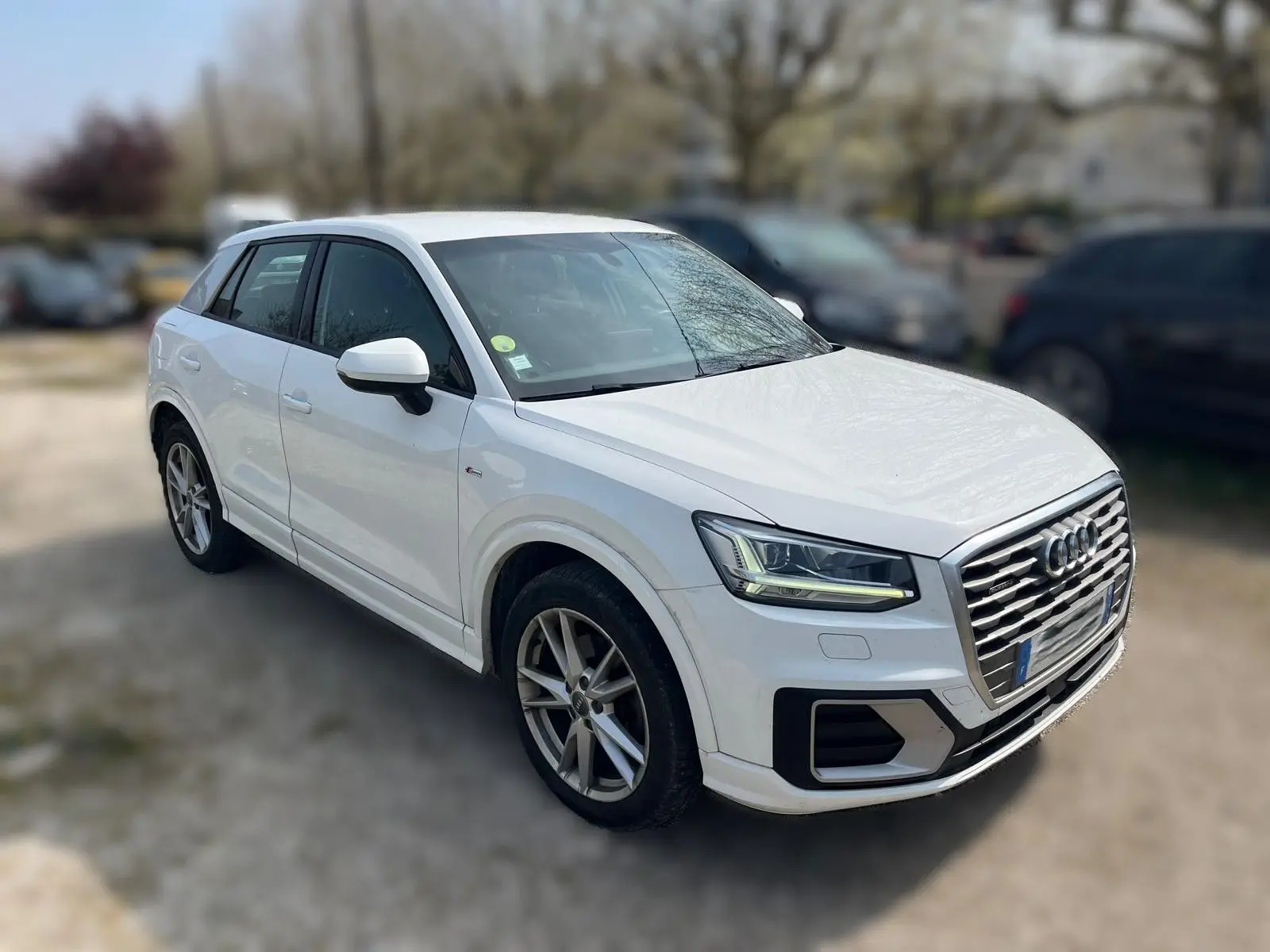 Audi Q2 blanc vue 3/4 avant droit, avec jantes alliage et calandre distinctive S-Line.