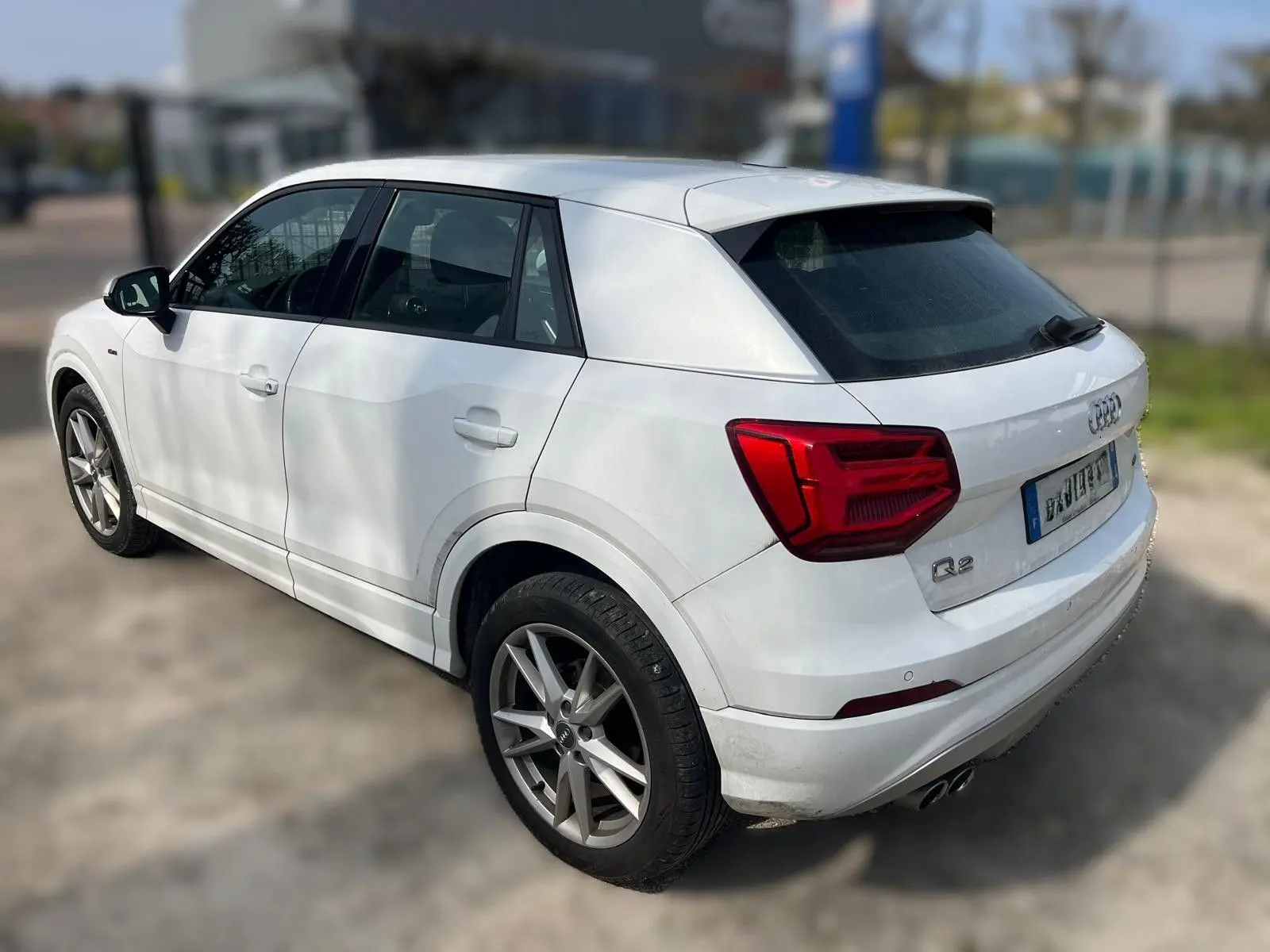Audi Q2 blanc vue 3/4 arrière droit, avec jantes alu et feux arrière rouges distinctifs.