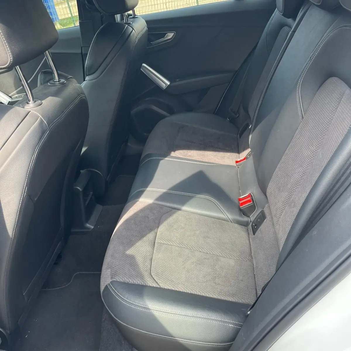 Vue intérieure côté arrière droit de l'Audi Q2 blanc, montrant la banquette en cuir et tissu noir avec ceintures rouges.