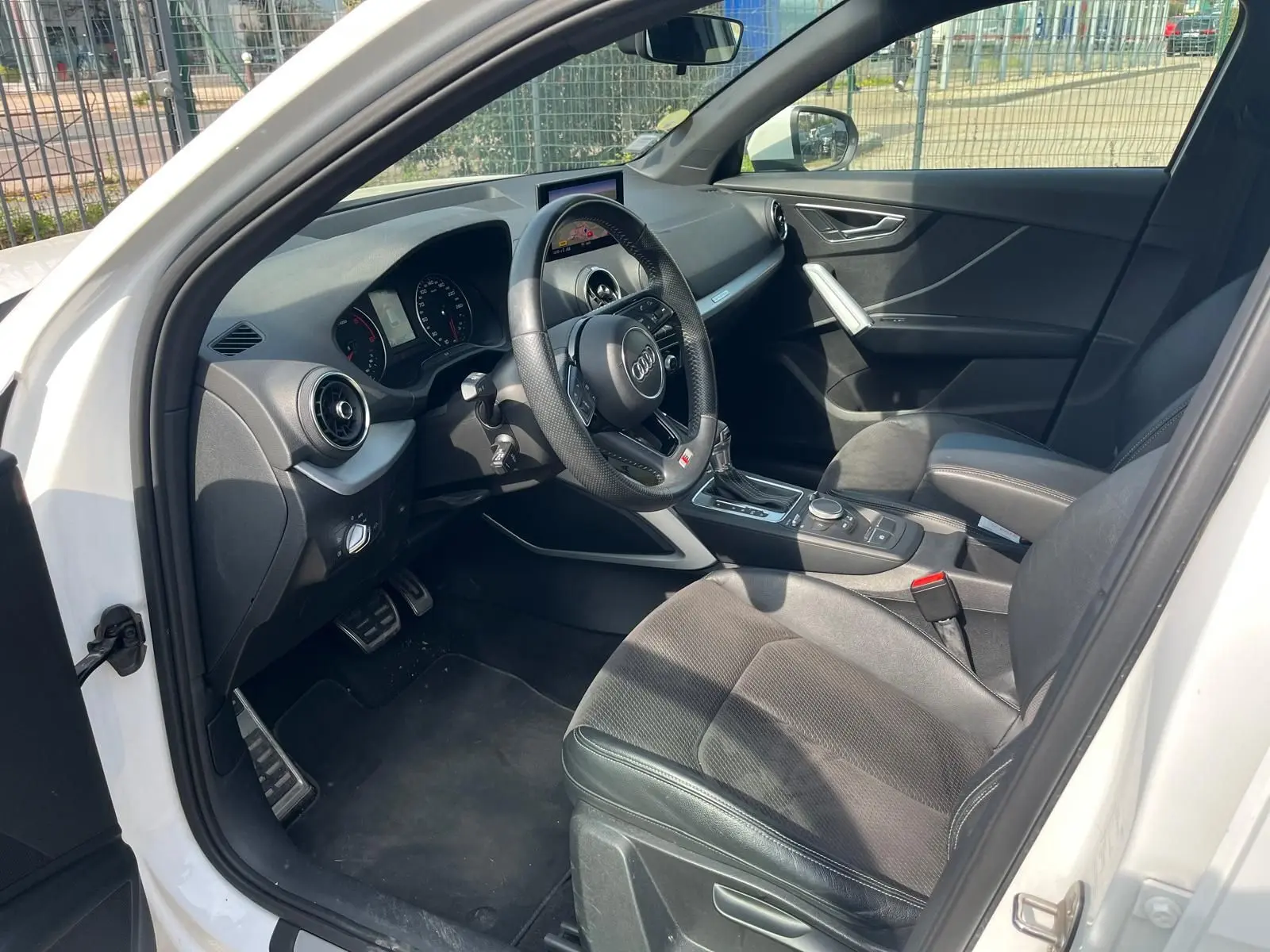 Vue intérieure côté conducteur de l'Audi Q2 blanche 2018, avec volant multifonction et sellerie noire en tissu et cuir.