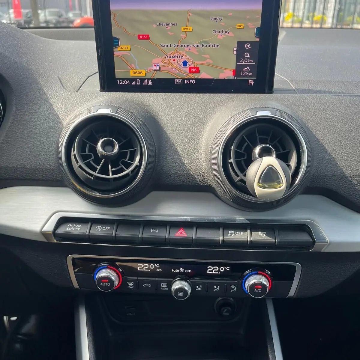 Vue rapprochée du tableau de bord de l'Audi Q2 blanc, avec écran GPS central et commandes de climatisation automatique.