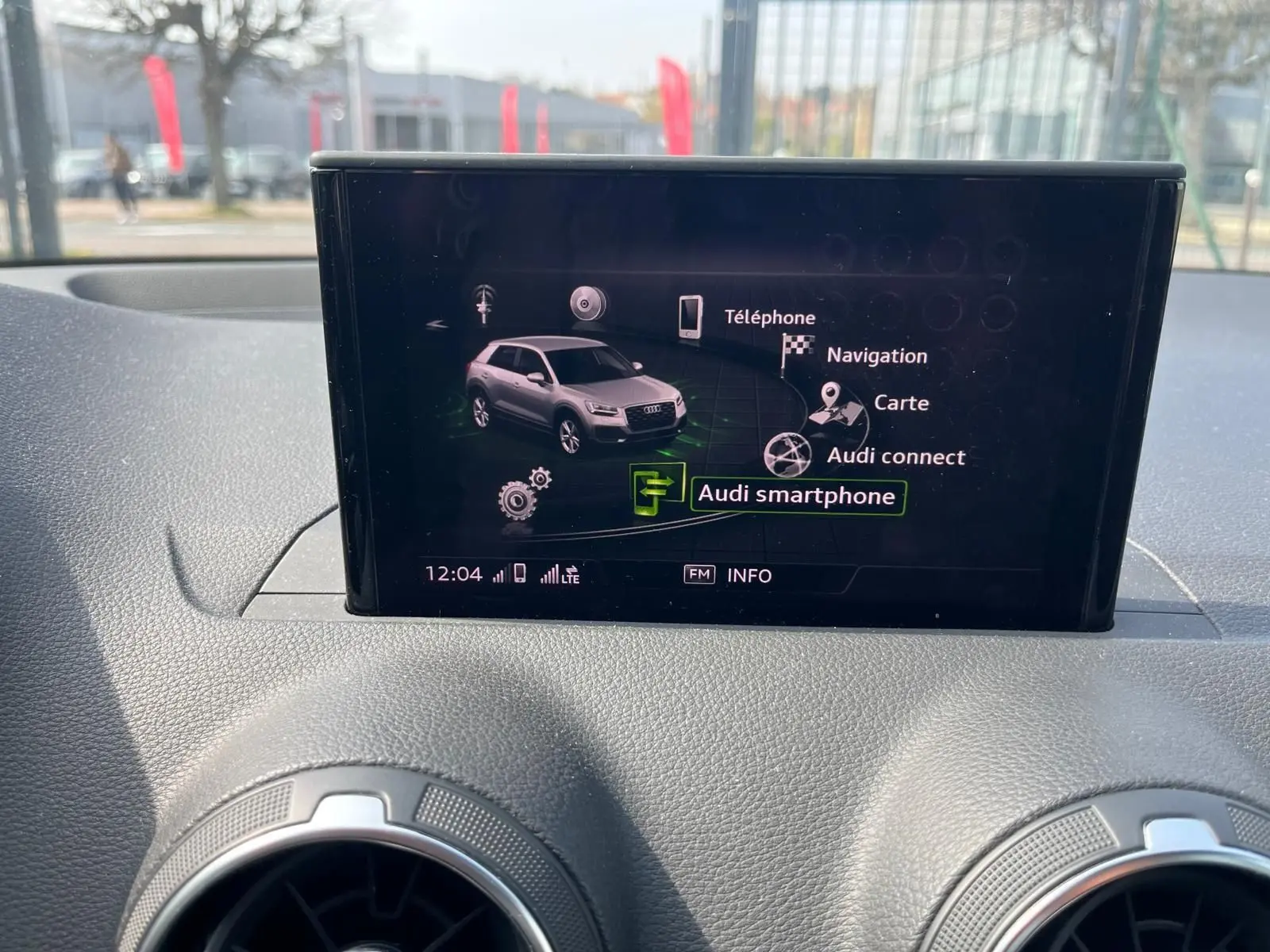 Écran central de l'Audi Q2 montrant le menu Audi smartphone avec vue intérieure sur tableau de bord noir.