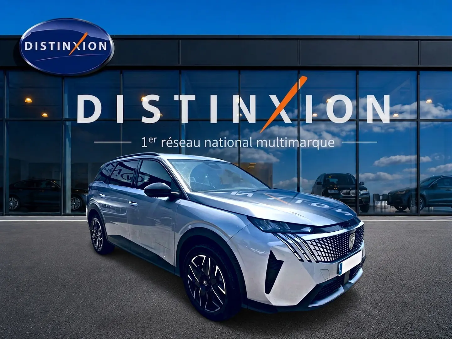 Peugeot 5008 Hybrid 145 gris Artense en 3/4 avant droit, avec calandre distinctive et jantes alu noires.