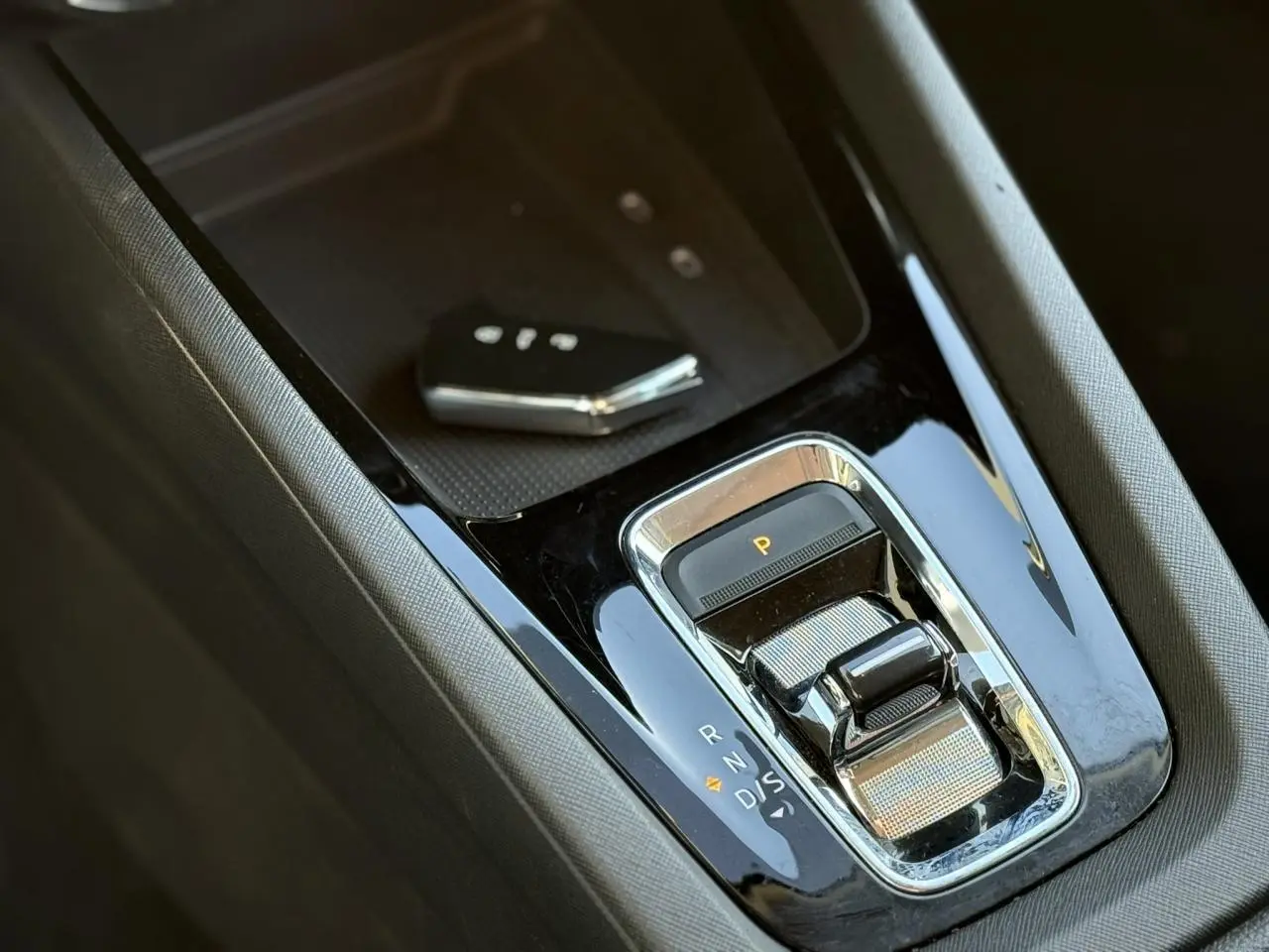 Gros plan sur la console centrale noire brillante de la Skoda Octavia Combi 2022 avec levier de boîte auto et clé main-libre.