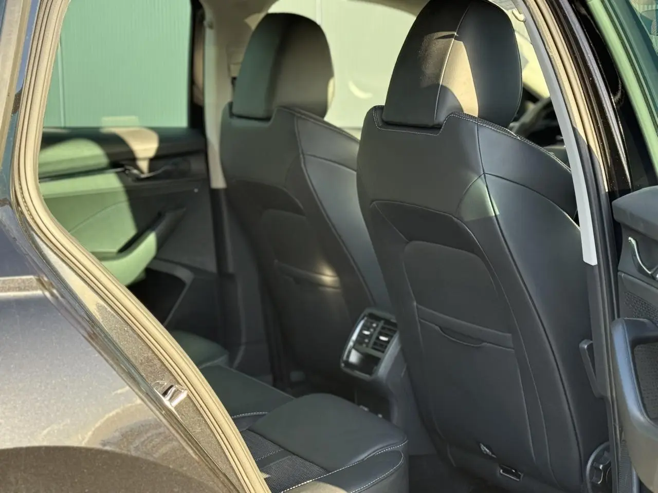 Vue intérieure arrière côté gauche d'une Skoda Octavia Combi noire 2022 avec sièges cuir noirs et aérateurs centraux.