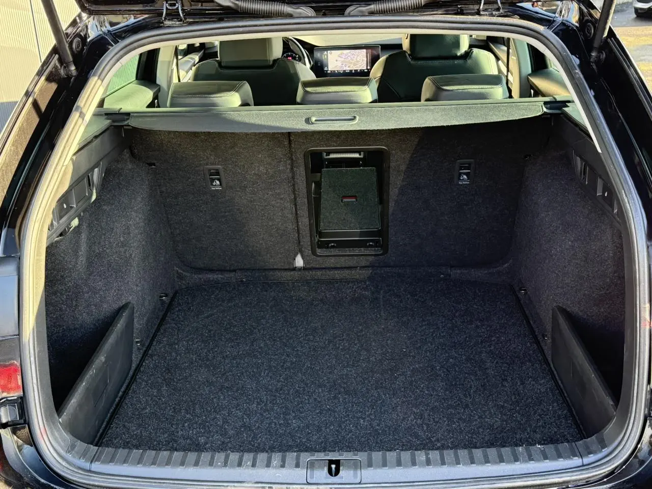 Coffre ouvert vu de l'arrière d'une Skoda Octavia Combi noire, avec tapis de sol gris et banquette arrière visible.