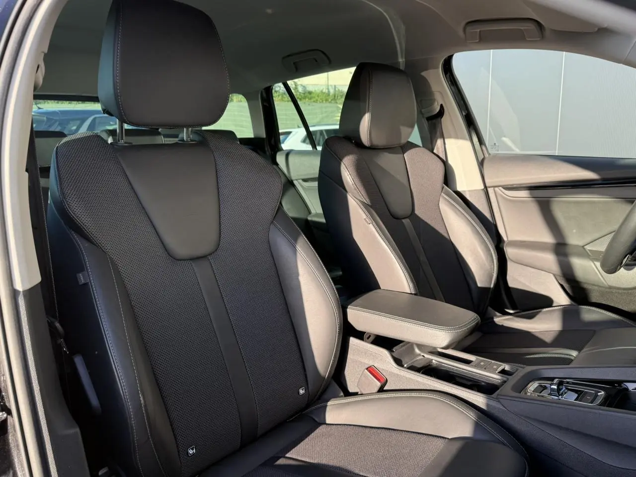 Vue intérieure sur les sièges avant en cuir/tissu noir de la Skoda Octavia Combi 2022 avec accoudoir central et console.