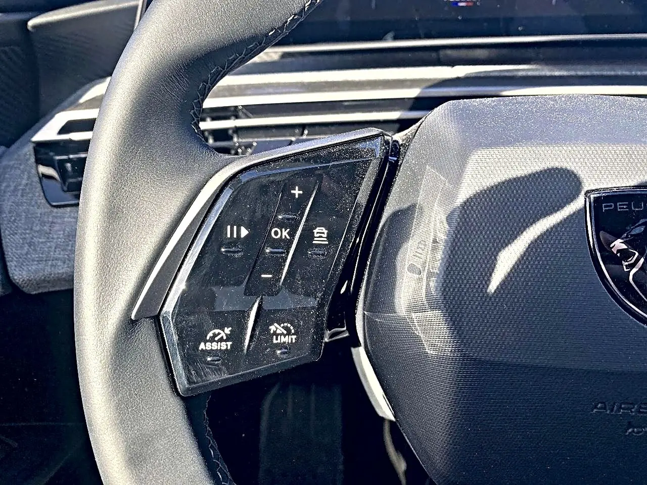 Gros plan sur le volant cuir noir de la Peugeot 5008 Hybrid 145 allure, avec commandes multifonctions à gauche.