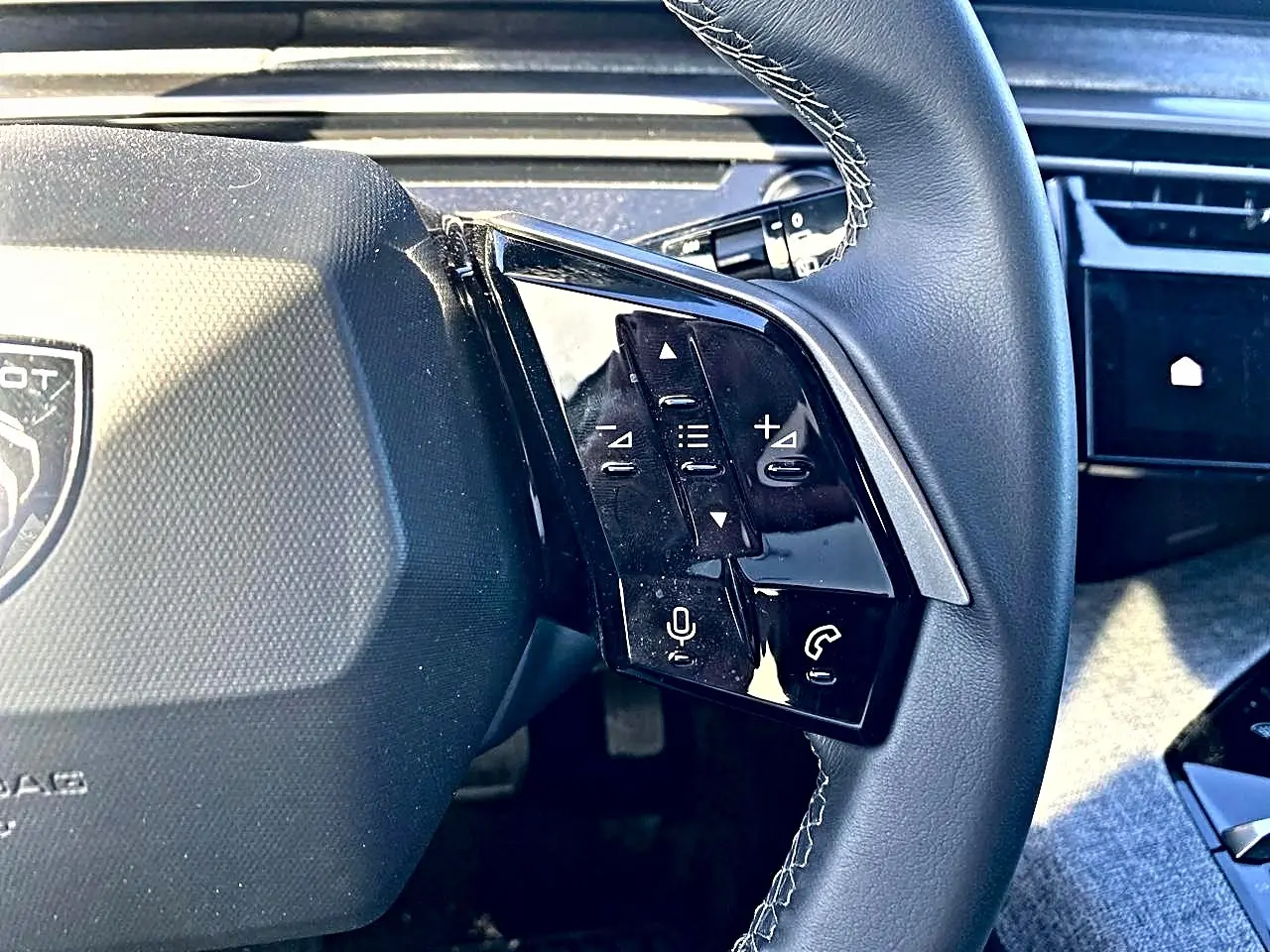 Gros plan sur le volant cuir noir du Peugeot 5008 Hybrid 145 avec commandes vocales et téléphone intégrées.