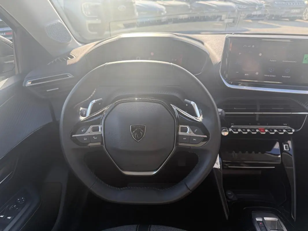 Vue intérieure centrée sur le volant noir de la Peugeot 208 Hybrid 110 e-DCS6 Allure 2024 avec tableau de bord et écran tactile.