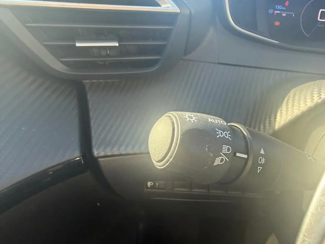 Gros plan sur la commande des phares à gauche du volant dans l’habitacle de la Peugeot 208 Hybrid 110 e-DCS6 Allure 2024.