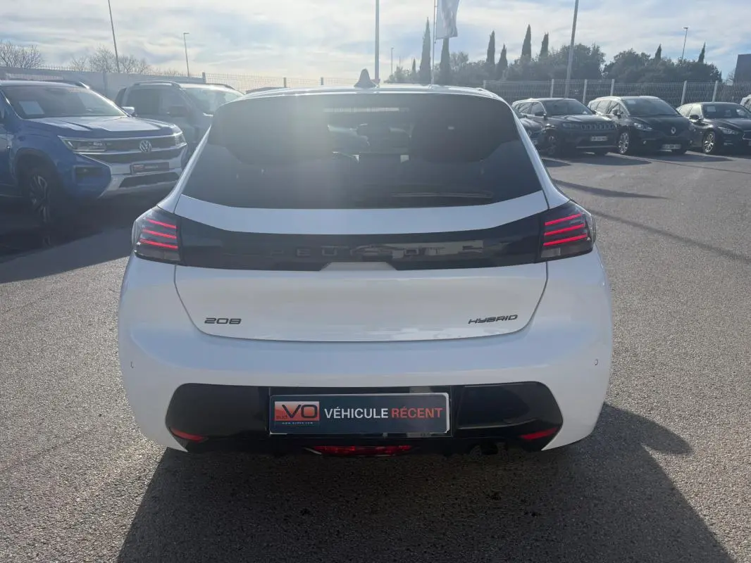 Vue arrière d'une Peugeot 208 Hybrid blanche 2024 avec feux LED distinctifs et plaque "Véhicule récent" visible.