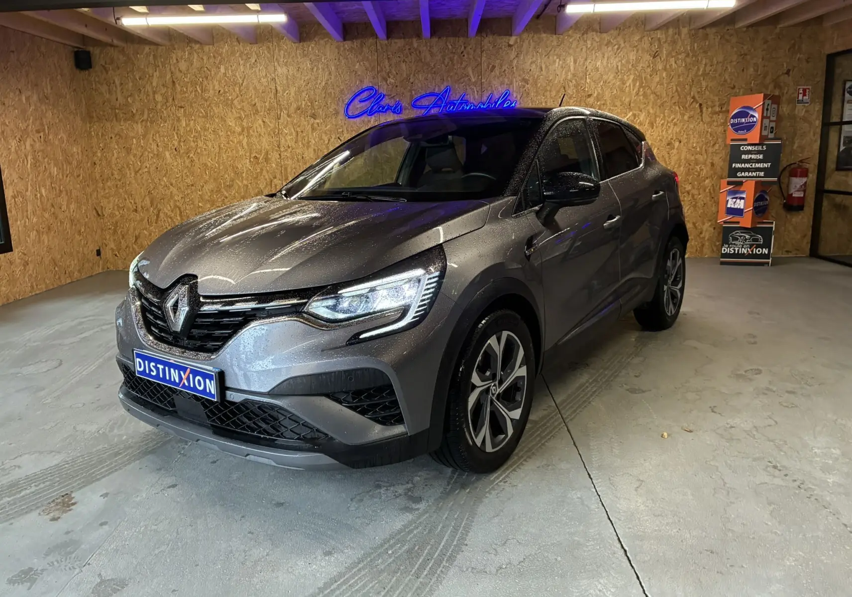 Renault Captur gris 3/4 avant droit en intérieur, avec phares allumés et jantes distinctives RS Line.