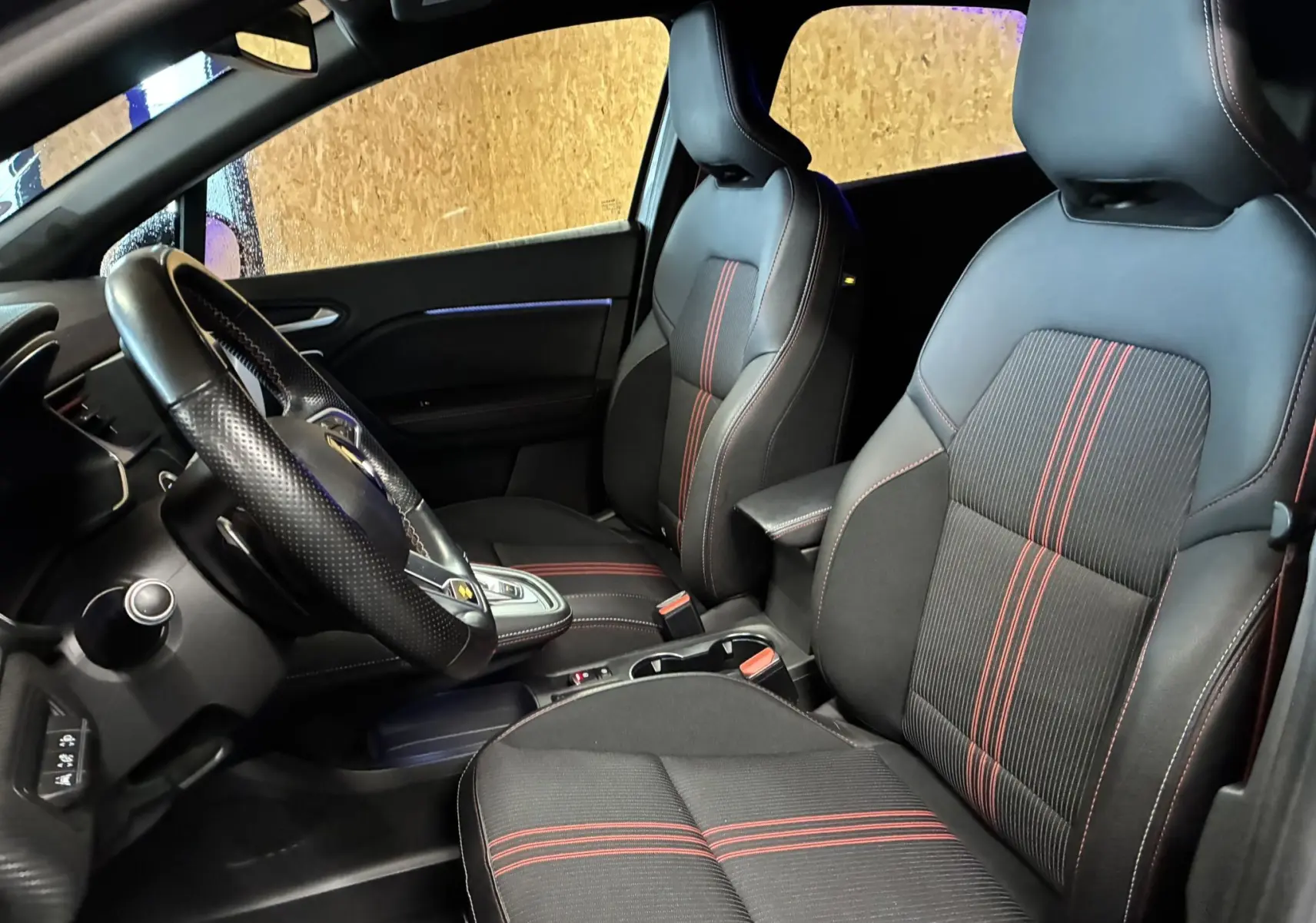 Vue intérieure côté conducteur du Renault Captur gris 2021, sièges tissu noir avec surpiqûres rouges et volant cuir perforé.