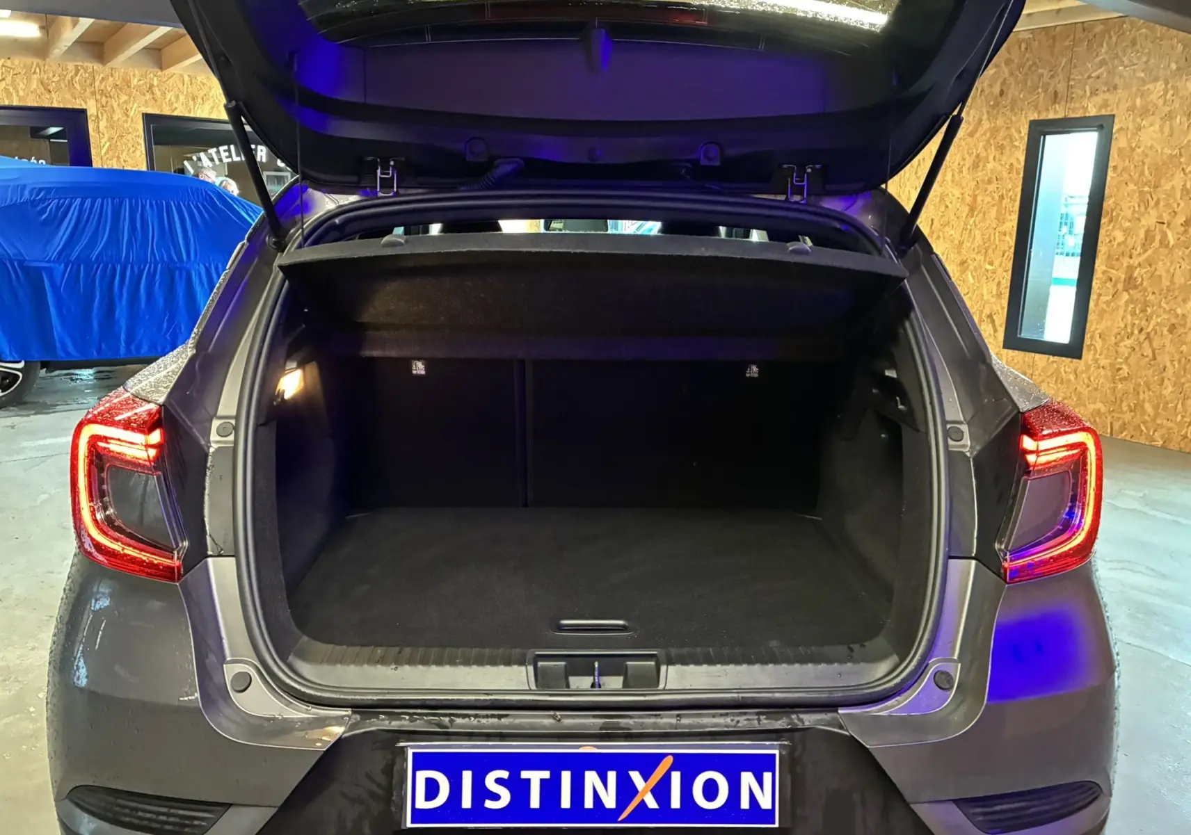 Vue arrière du coffre ouvert d’un Renault Captur gris 2021 avec feux arrière allumés dans un garage.