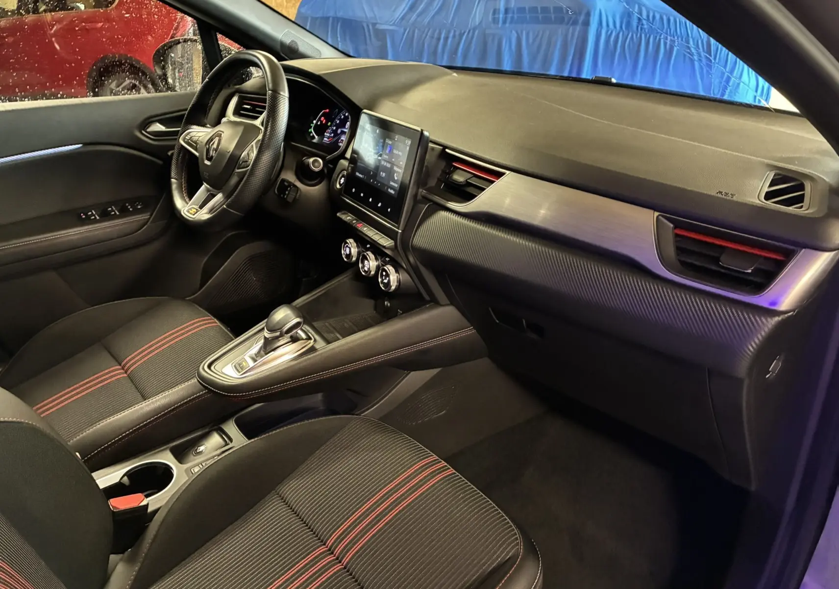 Vue intérieure côté conducteur du Renault Captur gris 2021, avec sièges tissu noirs à surpiqûres rouges et console centrale moderne.