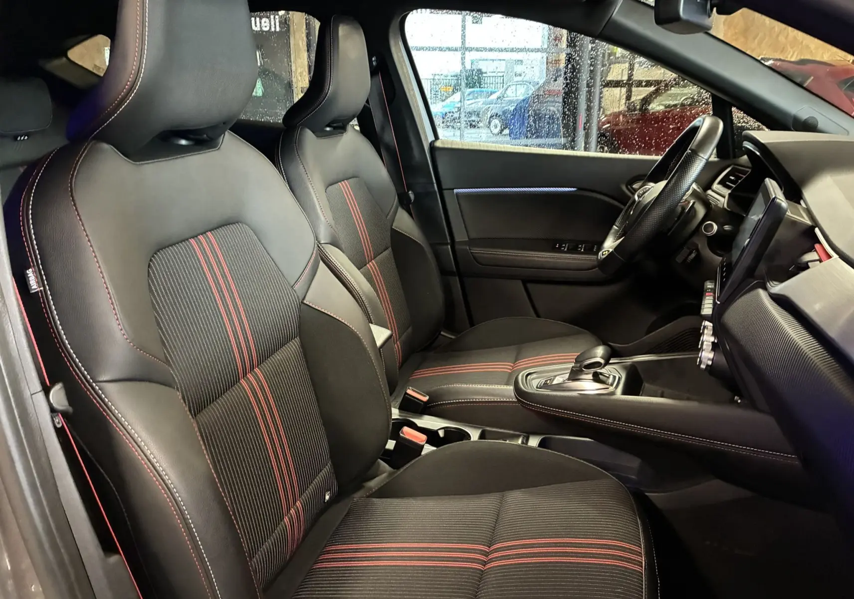 Vue intérieure côté conducteur du Renault Captur gris 2021, sièges tissu noir avec surpiqûres rouges et volant cuir.